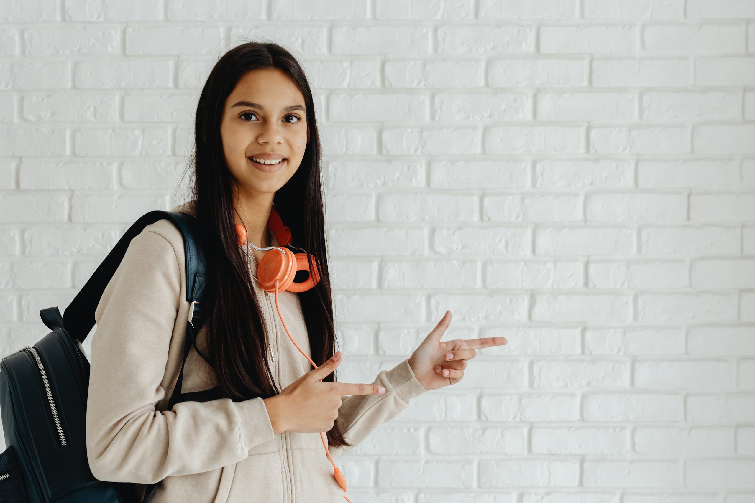 Smiling teenager with backpack and headphones pointing at something with enthusiasm.